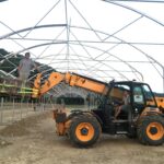 Photo des deux associés, Carle et Jean, sur le tracteur à fourche téléscopique loué lors du montage de la serre. Jean est au volant, Carle sur la plateforme.